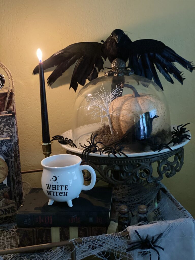 Halloween decorations bar cart white witch cauldron coffee mug crow on top of cake dome with pumpkin inside