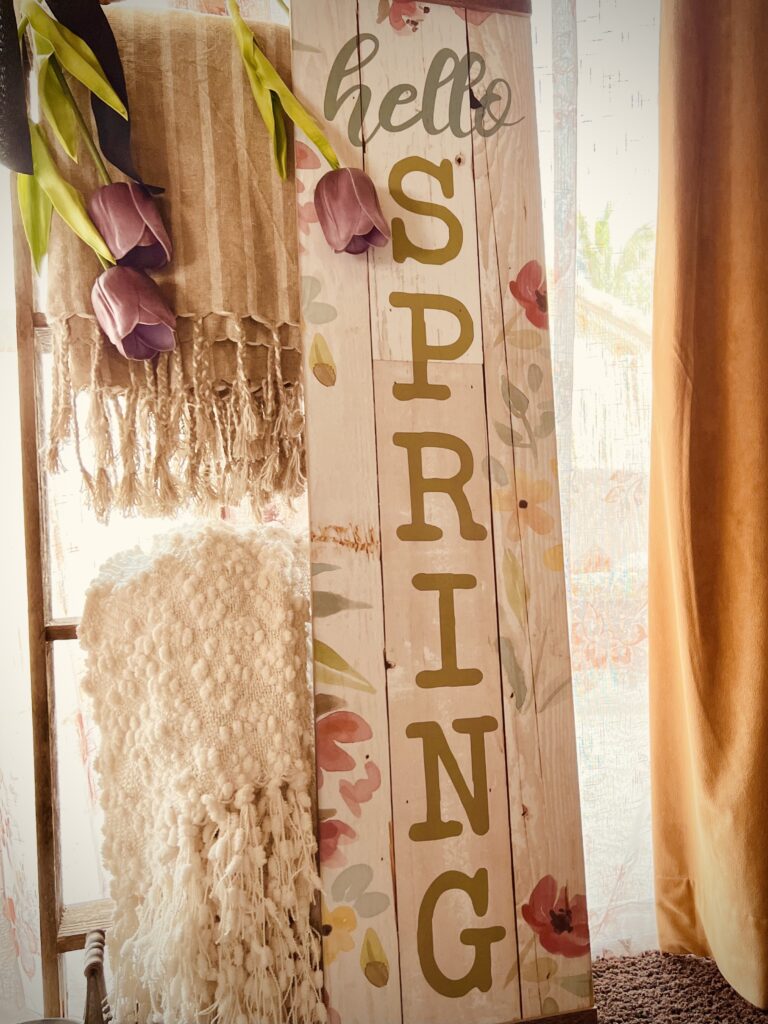 purple tulips draped over rustic ladder beige blankets with Spring wood sign